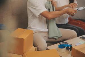 Two Asian blogger showing clothes in front of the camera to recording vlog video live streaming at her shop. Online Shopping Cart notion. on sofa at home photo