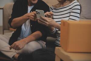 Two Asian blogger showing clothes in front of the camera to recording vlog video live streaming at her shop. Online Shopping Cart notion. on sofa at home photo