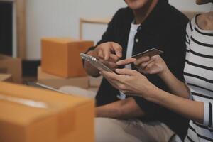Two Asian blogger showing clothes in front of the camera to recording vlog video live streaming at her shop. Online Shopping Cart notion. on sofa at home photo