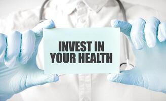 Doctor holding card in hands and pointing the word INVEST IN YOUR HEALTH photo