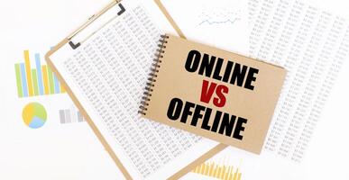 Text ONLINE VS OFFLINE on brown paper notepad on the table with diagram. Business concept photo