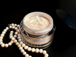 Translucent mineral powder with pearls necklace on black background. Natural cosmetics. Cosmetic product swatch. photo