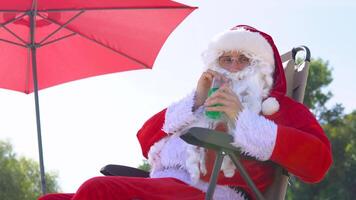 Santa Claus drinks a cocktail while lying on a sun lounger on the beach video