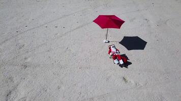 Santa claus ist Lügen auf ein Sonne Liege auf das sandig Strand. oben Sicht. Kamera ziehen um zu das Rechts. Santa im das Tropen video