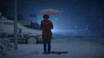 jung afrikanisch Frau Stehen auf Straße beim Nacht während Schnee fallen mit Regenschirm video