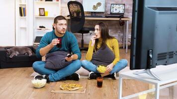 Couple sitting on the floor watching tv while the cat is sleeping. Man using tv remote control and drinking soda. video