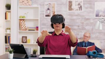 retirado mayor mujer asombrado mientras utilizando virtual realidad gafas de protección en vivo habitación. mayor hombre sentado en sofá mientras leyendo un libro. video