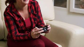 Single woman sitting on sofa playing video games using wireless controller.