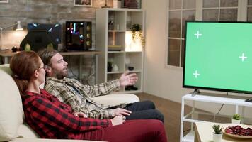 Hipster Paar Sitzung auf Sofa im Vorderseite von Fernseher mit Grün Bildschirm. heiter Beziehung. video