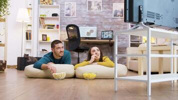 Couple talking with each other watching tv sitting on the pillows for the floor while their cat is relaxing in the background. video