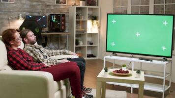 casado joven Pareja relajante en sofá acecho televisión con verde pantalla. video