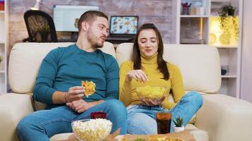 glad skäggig man skrattande medan tittar på en film med hans flickvän och äter pizza. popcorn och soda på kaffe tabell. video