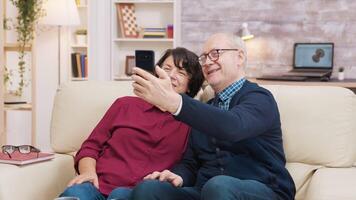 feliz Senior casal sentado em sofá levando uma selfie dentro a vivo quarto video