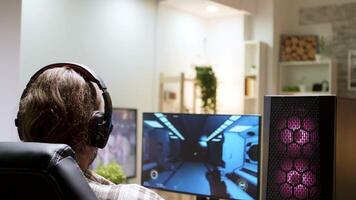 Over shoulder shot of man with long hair playing shooter games sitting on gaming chair. video