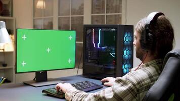 proffs skäggig gamer med lång hår spelar video spel på dator med grön mock-up.