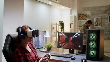 Side view of woman with red hair wearing vr goggles while playing video games with wireless controller.