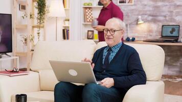 ouderen leeftijd paar met bril zittend Aan sofa gedurende een video telefoontje Aan laptop. oud paar gebruik makend van modern technologie