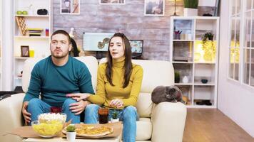 Disappointed couple after their favorite football team lost the game. Cat laying on sofa. Popcorn, pizza and soda on coffee table. video