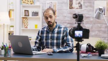 Famous young vlogger typing on laptop while talking with his subscribers on a podcast. Creative content creator. video