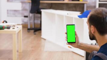 costas Visão do masculino trabalhador segurando telefone com verde tela. profissional mobília montagem trabalhador. video