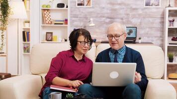 Elderly couple sitting on sofa using laptop for online shopping. Coffee on the table. video