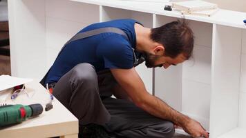 manlig arbetstagare använder sig av en skruvmejsel för möbel hopsättning i levande rum. man bär overall. video