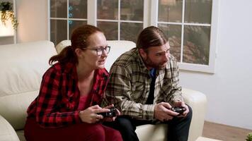 Hipster couple upset because their lose while playing video games using wireless controller.