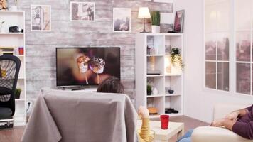 Back view of sitting on chair eating chips while watching tv with her boyfriend. video