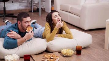 rilassato coppia seduta su il pavimento mangiare Pizza e patatine fritte mentre Guardando tv. video