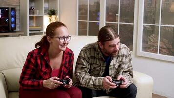 Hipster couple sitting on sofa playing video games using wireless controller. Man and woman giving high five.