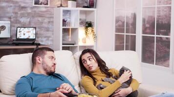 Tired man using tv remote control sitting on the couch while his girlfriend is playing with the cat. video