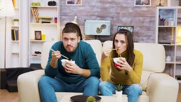 Couple sitting on couch eating noodles with chopstick and watching tv. video