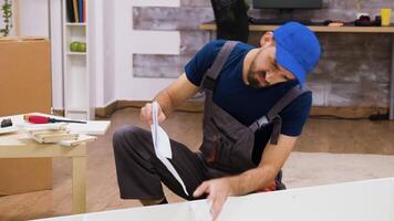 Confused worker in overalls reading instructions for furniture assembly wearing a cap. video