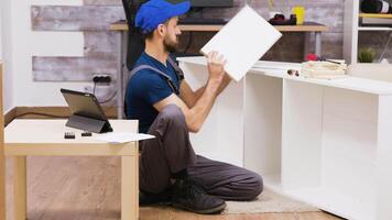 mannetje arbeider in overall met een pet bijeenkomst een plank in nieuw huis in aansluiting op instructie van tablet computer video