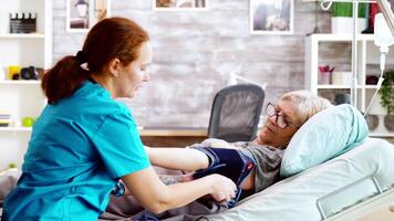 In nursing home old lady gets her blood pressure checked by an young caucasian nurse. Bright room with big windows video