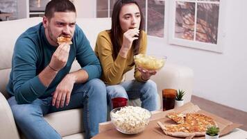 assustado casal depois de uma assustador momento dentro a filme a partir de televisão. casal sentado em sofá comendo pizza. video