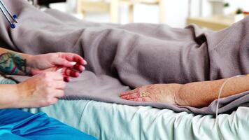 Close up shot of young caucasian assitant taking the hand of an old lady lying in hospital bed. video