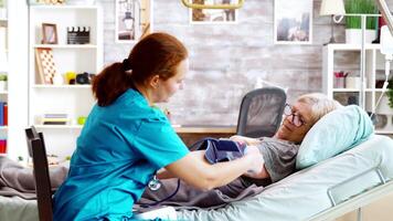 Nurse measuring blood pressure of old sick lady laying in hospital bed in a retirement home video