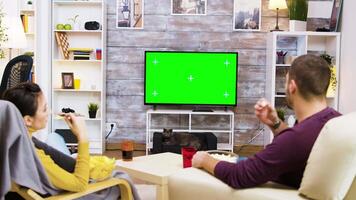 Back view of couple watching tv at home green screen, eating popcorn and the cat looking at them. video