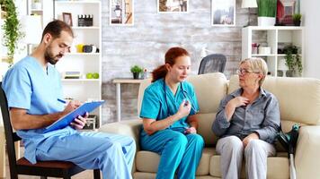 Male assistant taking notes on clipboard while female doctor is talking with senior woman in nursing home video