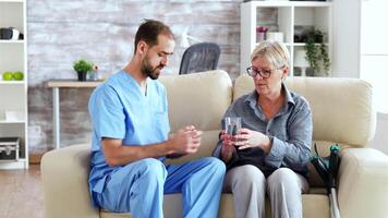 männlich Krankenschwester Sitzung auf Couch mit Senior Frau geben ihr medizinisch Behandlung im Pflege- heim. video