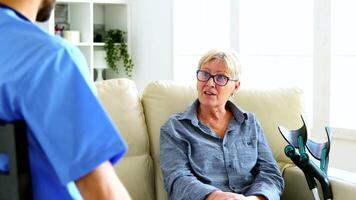 männlich Krankenschwester und Senior Frau haben ein Konversation im Pflege- heim. Alten im Ruhestand Frau mit Krücken Sitzung auf das Couch video