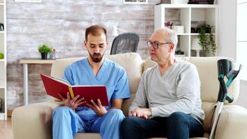 Social worker reading a book to an old disabled man in nursing home. video