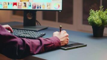 Close up of photographer using graphic tablet to retouch photos during night time in his office. video