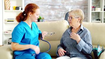 Caregiver woman in nursing home checking on old retired lady. Nurse listening the heart rate with a stethoscope video