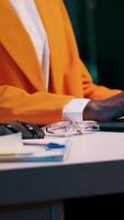 Vertical Video Portrait of african american student putting glasses on and working on english essays at home, reading academic databases for additional resources. Young woman studying at university. Camera A.