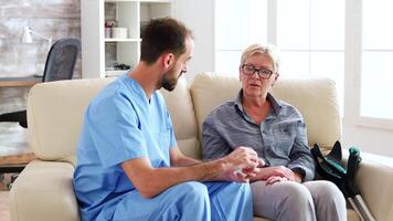 masculino médico asistente sentado en el sofá con mayor mujer narración acerca de su nuevo pastillas en enfermería hogar video