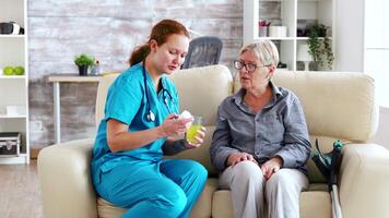 Female doctor sitting on sofa with senior woman in nursing home giving her daily pills. video