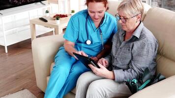 Female nuse helping senior elderly retired woman how to use her tablet computer in nursing home video