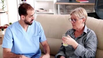 mayor retirado mujer en enfermería hogar con masculino médico hablando acerca de salud problemas mientras tomando su medicación video